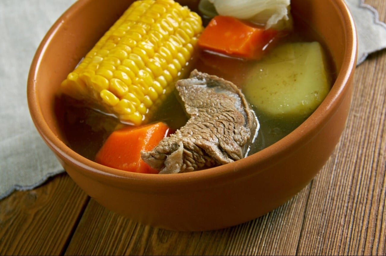 Cuban ajiaco served in a terracotta bowl with corn, meat, carrot and potato