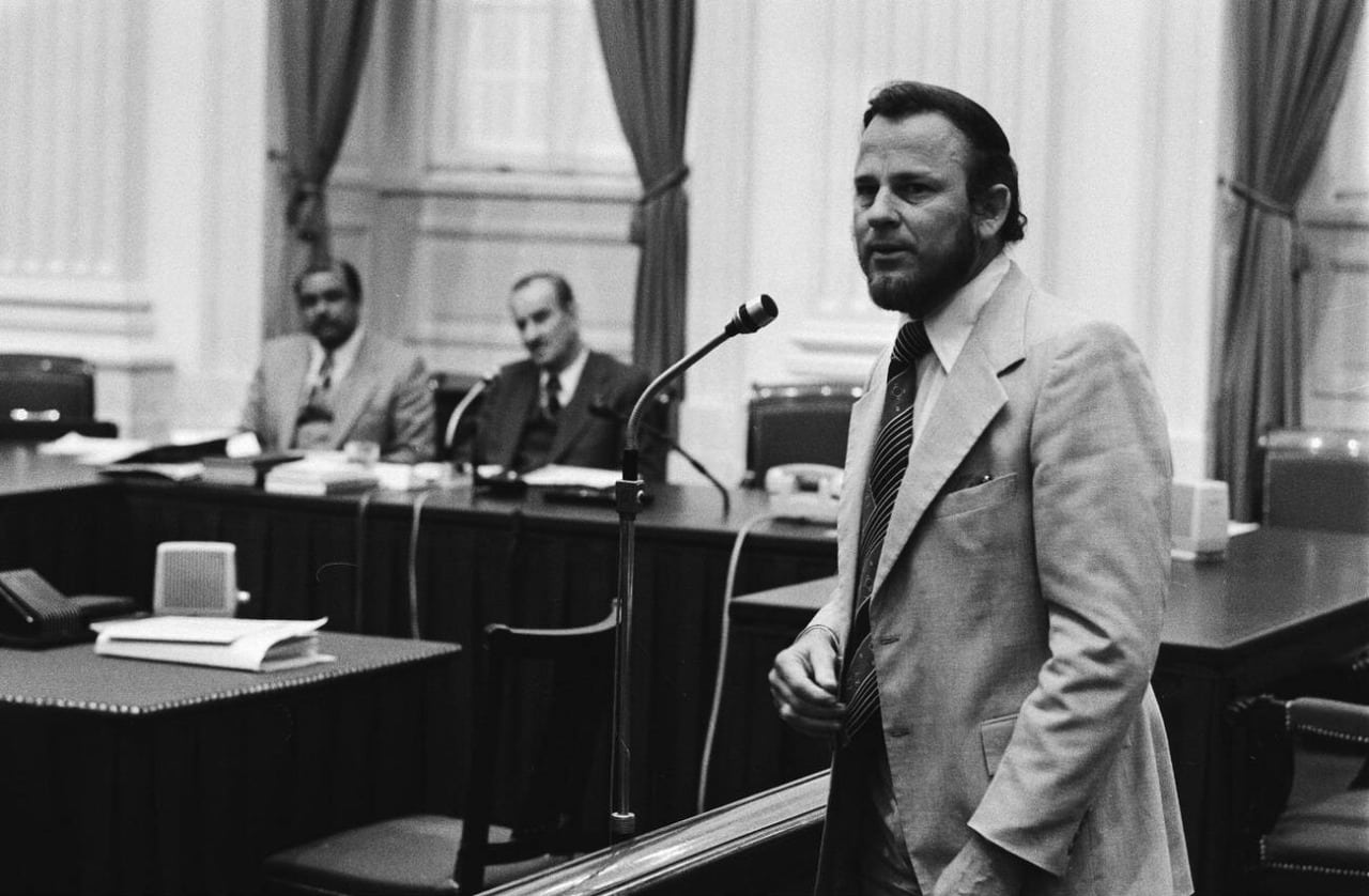 Betico Croes, in a light suit, standing in front of a microphone as he speaks