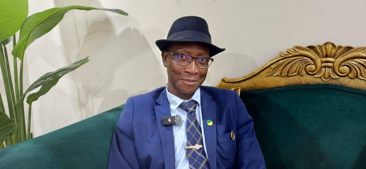 Portrait of Gabriel Serville, president of the Territorial Collectivity of French Guiana, wearing a blue suit and a hat, seated on a green sofa