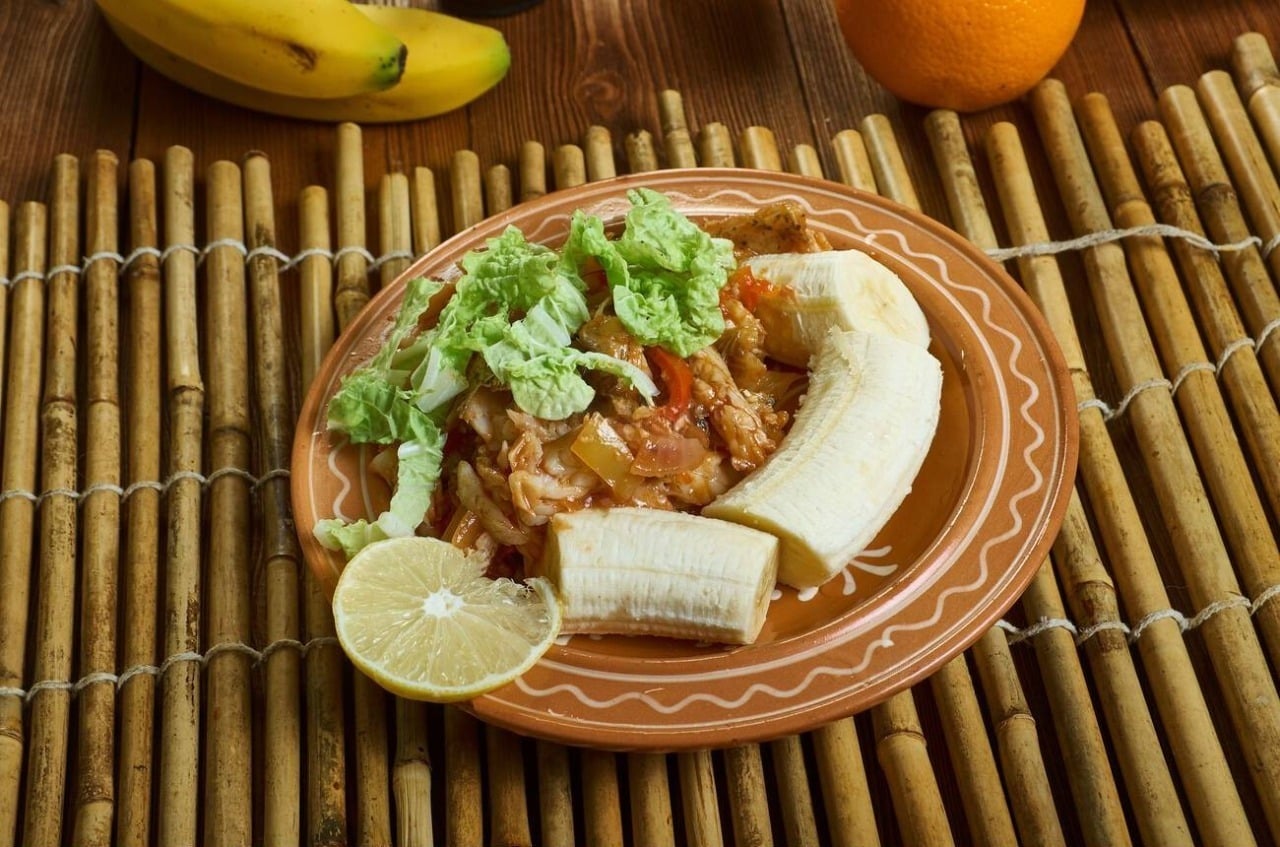 Plate of green fig and saltfish: green banana, salt cod and cabbage with a slice of lemon on a bamboo place mat